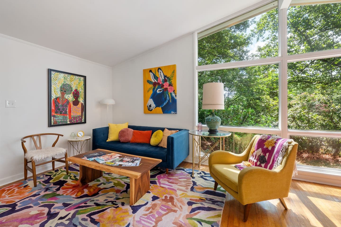 The Big Chill's front living room: a peacock-blue sofa and mustard armchair under a wall of mid-century glass